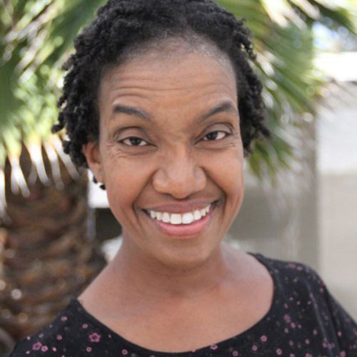 Headshot of Diana Elizabeth Jordan, a Black woman wearing a black top, short hair, and a bright smile, posing in front of a tree.