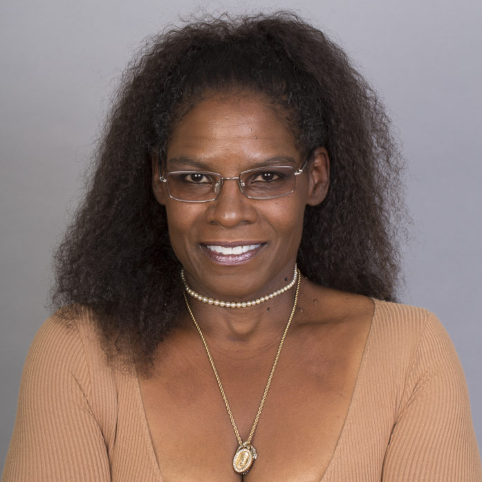 Headshot of Cheryl L. Bedford, a Black woman with long curly hair, wearing glasses, necklaces and a tan top.