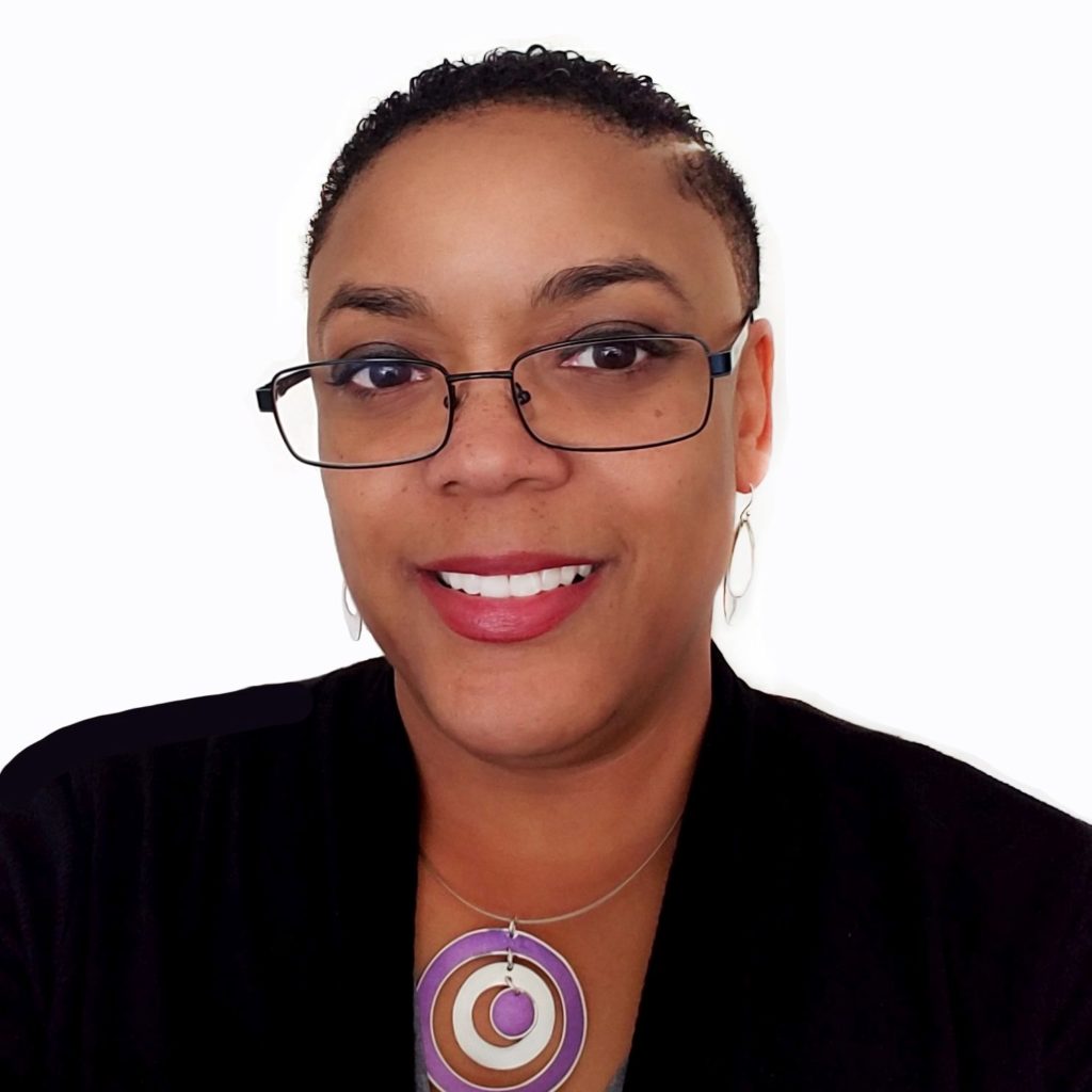 Headshot of Toni Y. Long, a Black woman posing in front of a white backdrop. She is wearing her hear tightly cropped, glasses, a black top and a necklace with large donut-shaped pendant, and a bright smile.