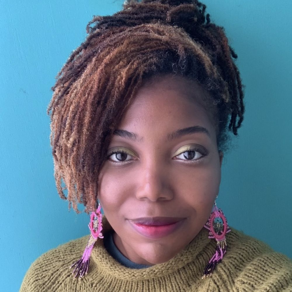 Headshot of Jordan Kauwling. Black woman with an updo, pink earrings and a beige knit sweater.